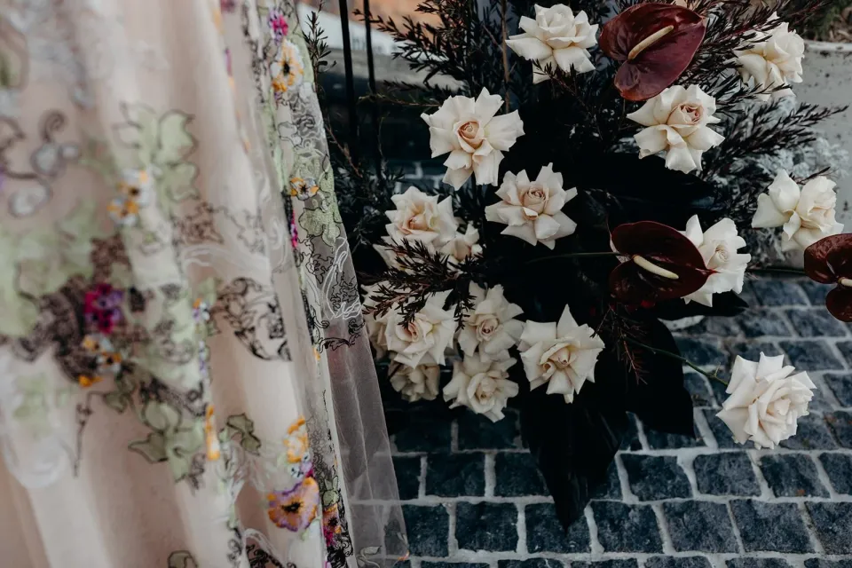 Detail of Victoria’s floral dress beside white blooms and burgundy flowers arranged by Mrs Gibbons Flowers, at Agnes Restaurant in Fortitude Valley, Brisbane, for an Elopement Collective elopement. Photo by Tessa Shannon.