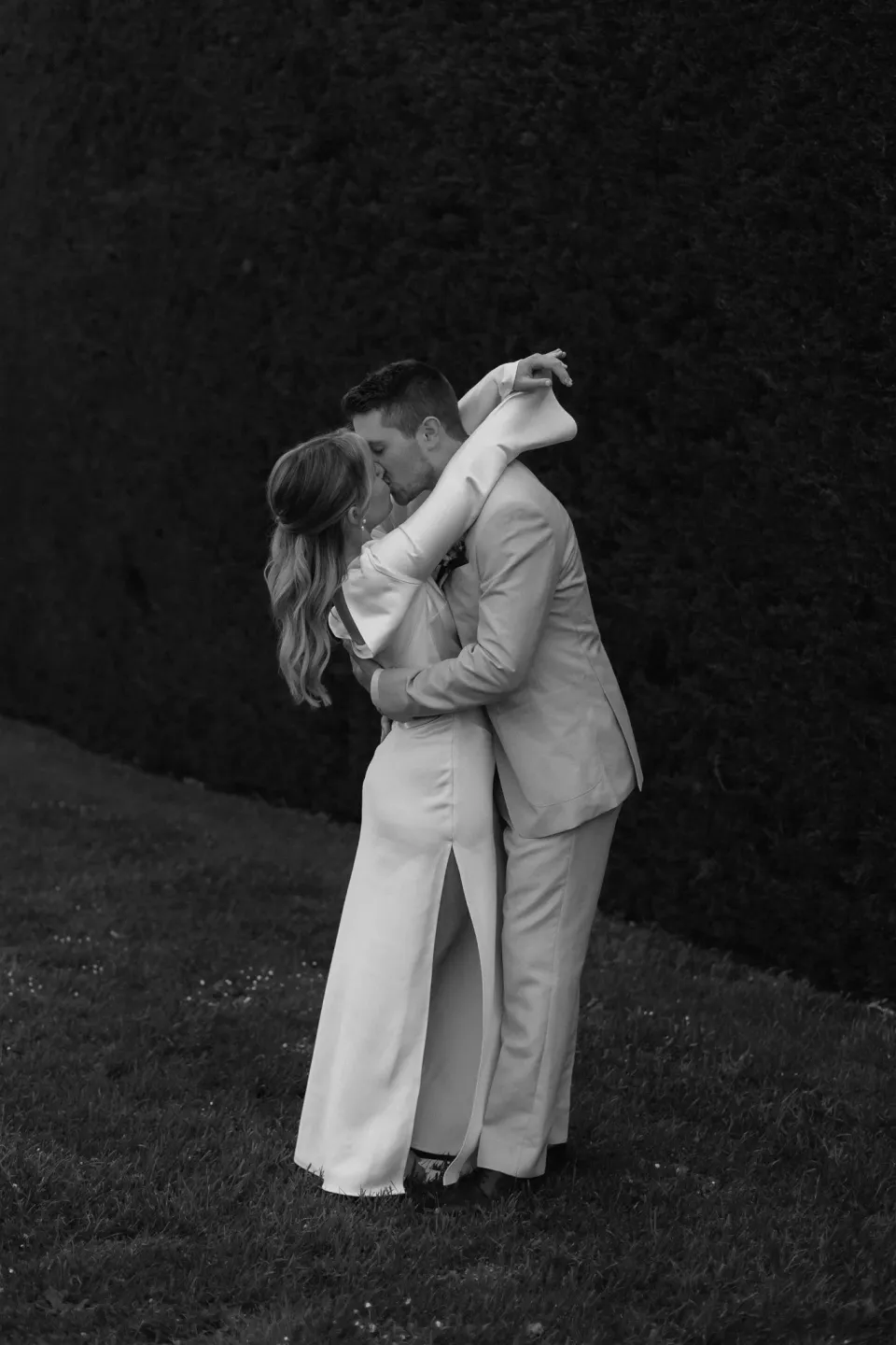 Black-and-white photograph of Maddy and Cameron holding each other close on the garden lawn, at The Mayor’s Residence in Daylesford, Victoria, for an Elopement Collective elopement. Photo by Bulb Creative.