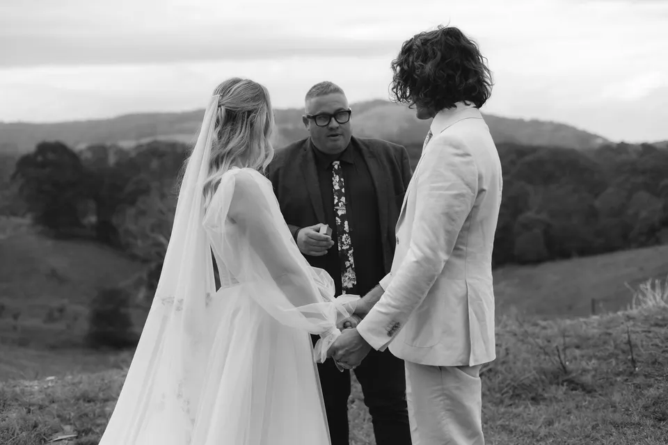 Black-and-white photograph of Josh Withers leading Bridget and James's ceremony. At Cudgera Creek in northern New South Wales, for an Elopement Collective elopement. Photograph by Bulb Creative.