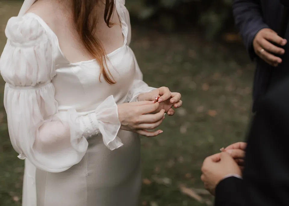 Elyse holding a wedding ring between her fingers. At Fig Tree Villa in Ewingsdale, Byron Bay, for an Elopement Collective elopement. Photograph by Bulb Creative.