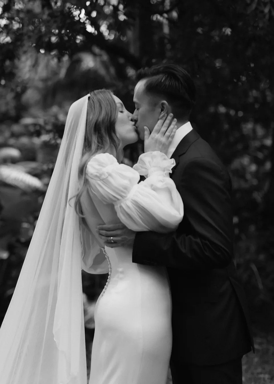 Black-and-white close portrait of Elyse kissing Jonathan. At Fig Tree Villa in Ewingsdale, Byron Bay, for an Elopement Collective elopement. Photograph by Bulb Creative.