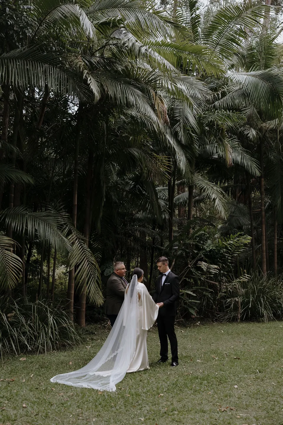 Wide view of Laura and Matthew's ceremony surrounded by tall palms and dense greenery. At Fig Tree Villa in Ewingsdale, Byron Bay, for an Elopement Collective elopement. Photograph by George Bowden.