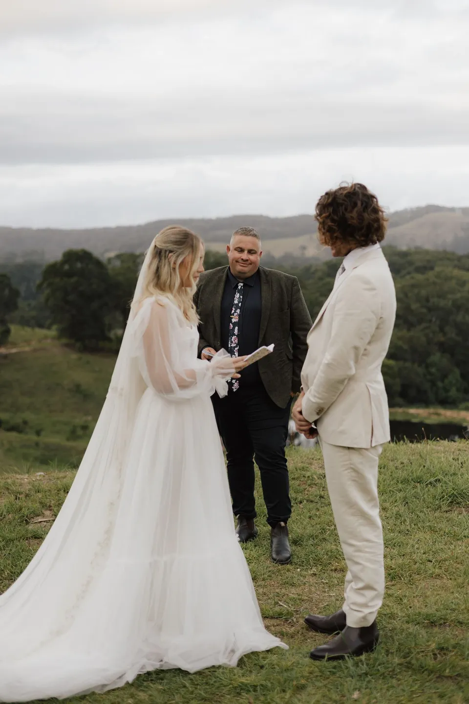 Bridget and James facing each other during their vows with Josh Withers between them. At Cudgera Creek in northern New South Wales, for an Elopement Collective elopement. Photograph by Bulb Creative.