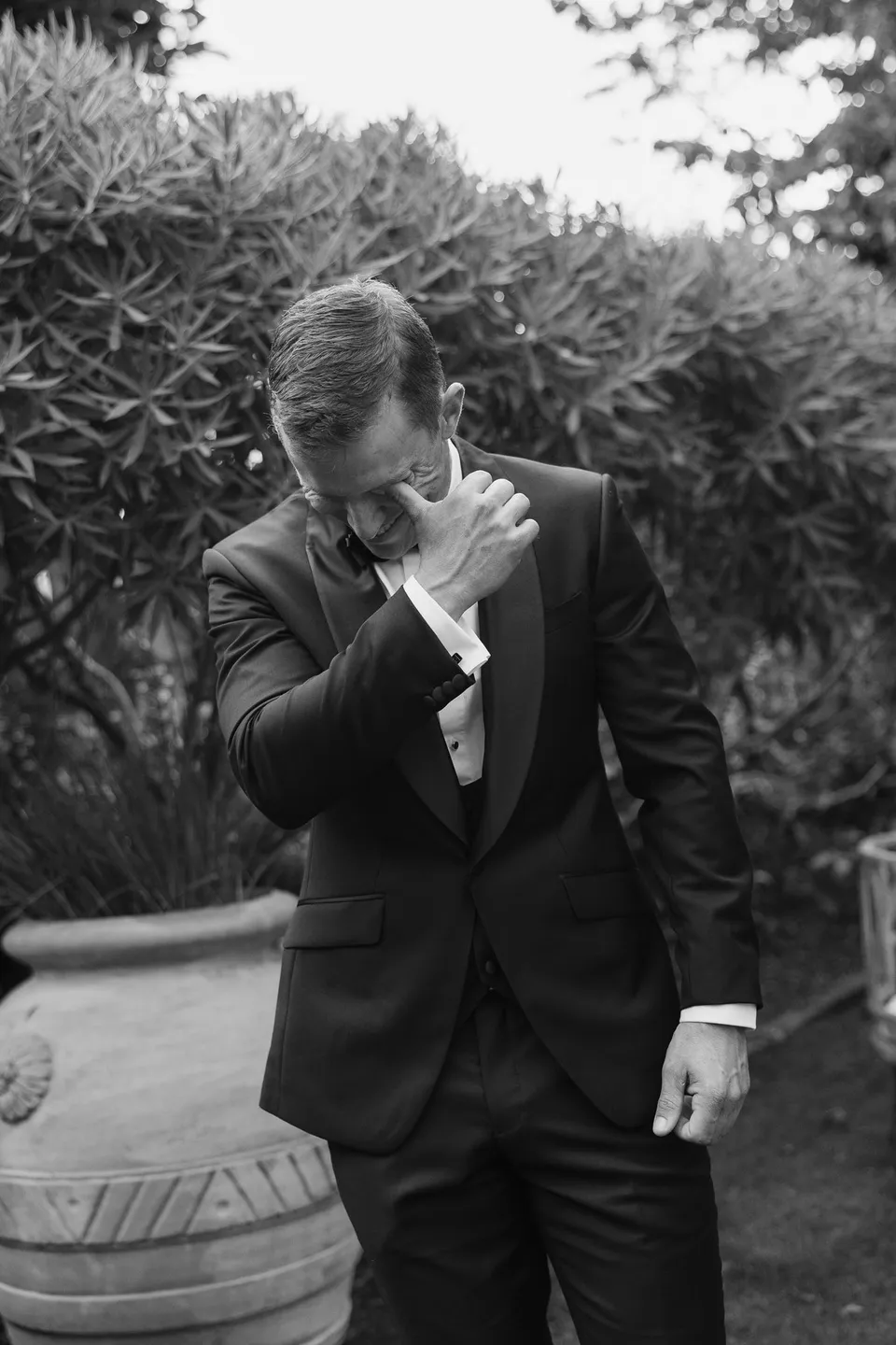 Black and white photograph of Andrew bringing a hand to his face while standing in the garden, at Islington Hotel in South Hobart, Tasmania, Australia, for an Elopement Collective summer elopement. Photograph by George Bowden.