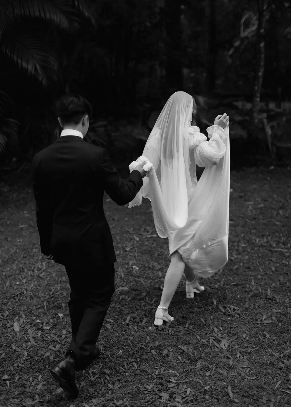 Black-and-white photograph of the couple walking away from their ceremony. At Fig Tree Villa in Ewingsdale, Byron Bay, for an Elopement Collective elopement. Photograph by Bulb Creative.