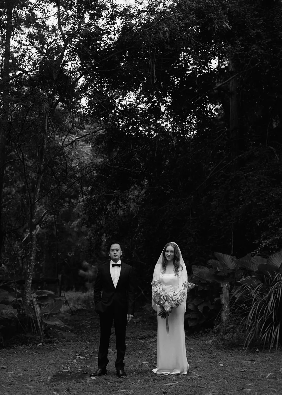 Wide black-and-white portrait of Elyse and Jonathan beneath the trees. At Fig Tree Villa in Ewingsdale, Byron Bay, for an Elopement Collective elopement. Photograph by Bulb Creative.
