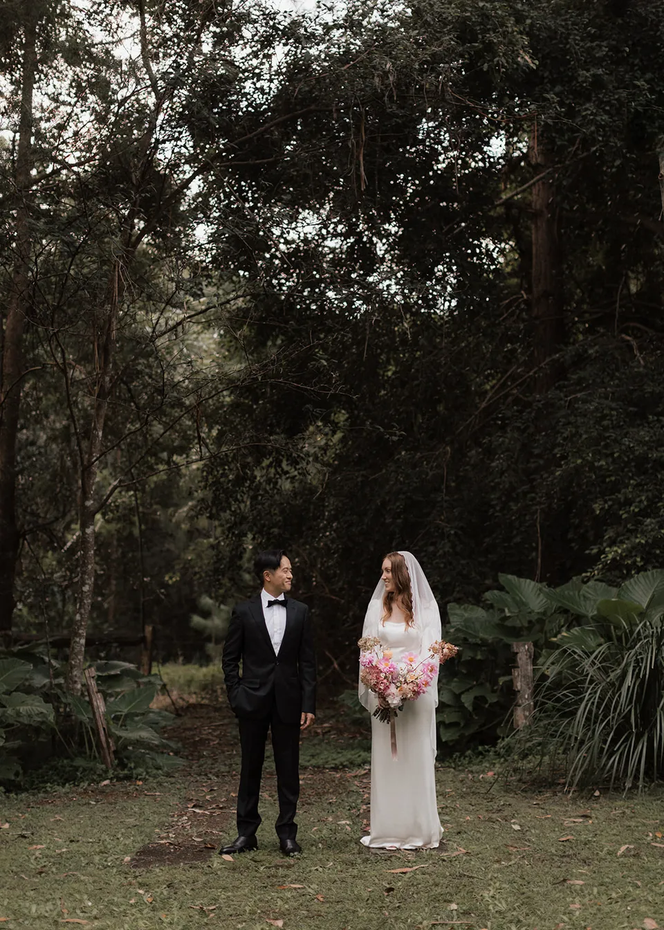 Distant portrait of the couple in a clearing surrounded by lush greenery. At Fig Tree Villa in Ewingsdale, Byron Bay, for an Elopement Collective elopement. Photograph by Bulb Creative.
