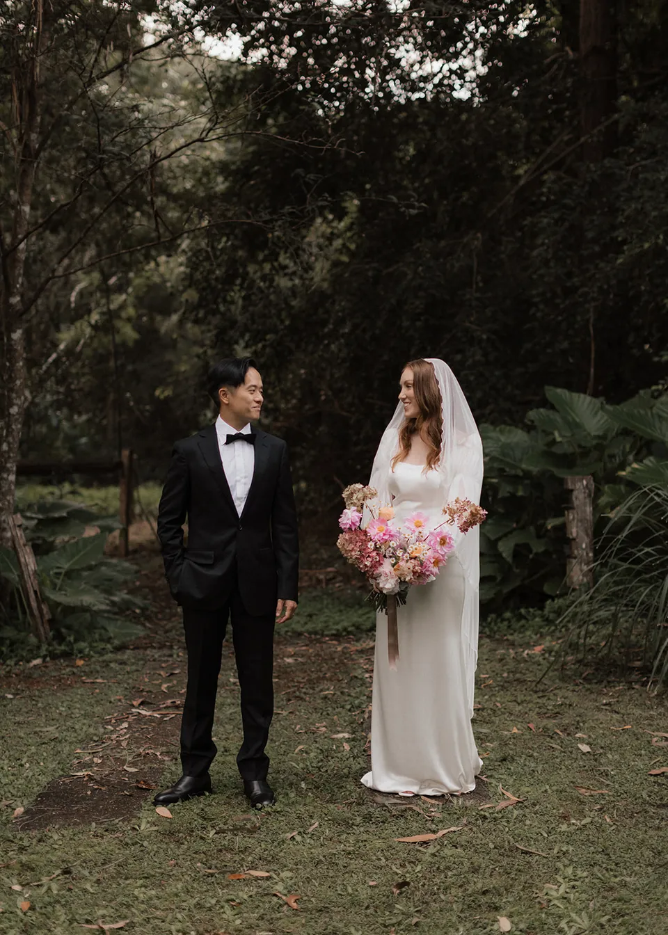 Elyse looking towards Jonathan as they stand on the lawn. At Fig Tree Villa in Ewingsdale, Byron Bay, for an Elopement Collective elopement. Photograph by Bulb Creative.