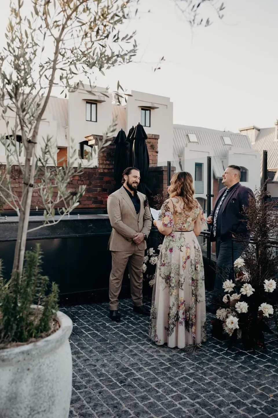 Victoria and Daniel exchanging vows with celebrant Josh Withers beside white flowers by Mrs Gibbons Flowers, at Agnes Restaurant in Fortitude Valley, Brisbane, for an Elopement Collective elopement. Photo by Tessa Shannon.