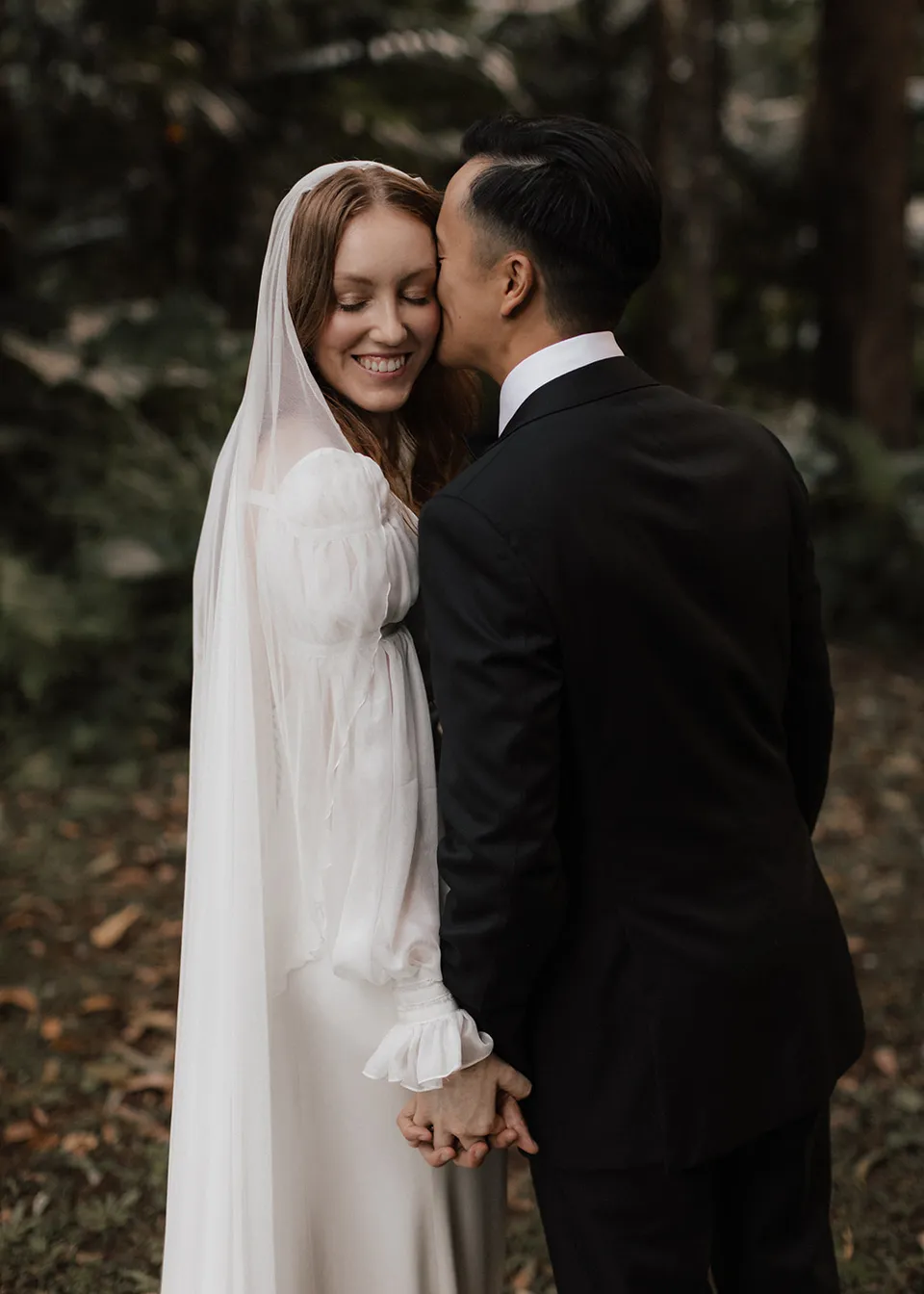 Elyse smiling with her eyes closed as Jonathan kisses her cheek. At Fig Tree Villa in Ewingsdale, Byron Bay, for an Elopement Collective elopement. Photograph by Bulb Creative.