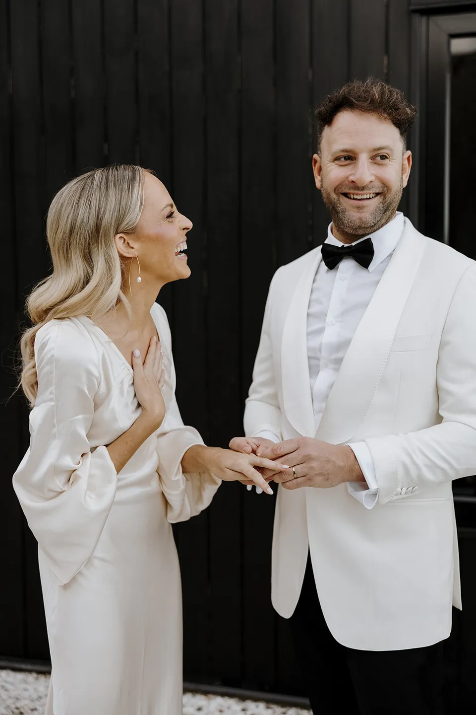 Greg smiling as Gabrielle looks towards him during their ring exchange beside the dark cabin, at Roundhill Retreat in Obi Obi, Sunshine Coast Hinterland, Queensland, for an Elopement Collective elopement. Photo by George Bowden.