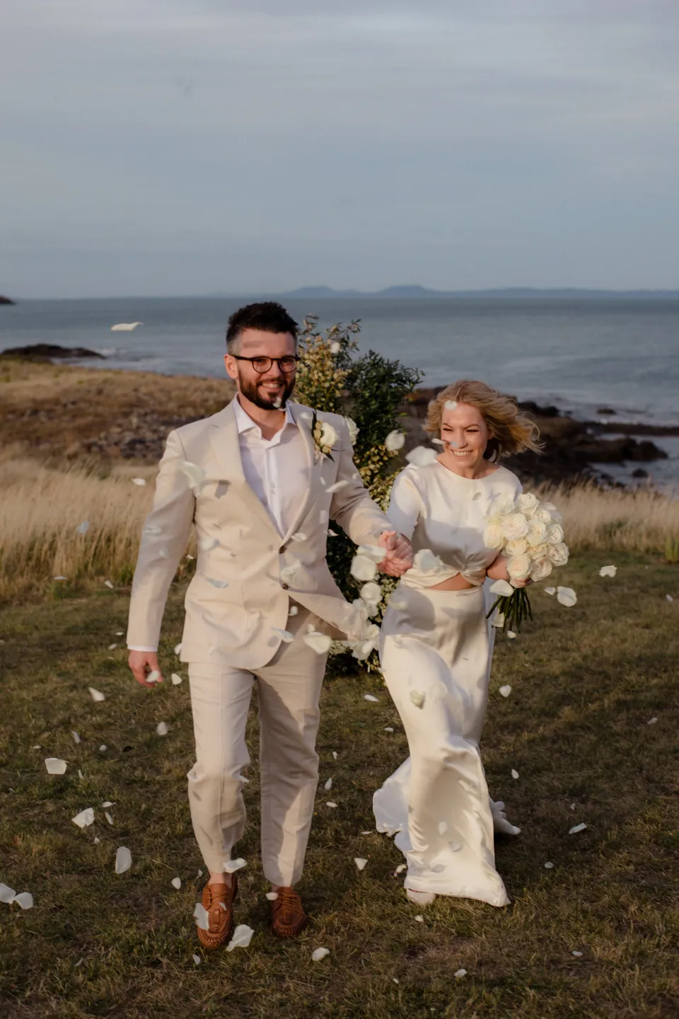 Jemmah and Jack smiling as they walk away from their ceremony, at Thalia Haven on the East Coast of Tasmania, Australia, for an Elopement Collective elopement. Photograph by Joey Willis.