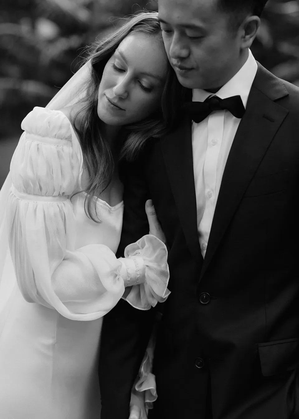 Black-and-white close portrait of Elyse resting her head against Jonathan. At Fig Tree Villa in Ewingsdale, Byron Bay, for an Elopement Collective elopement. Photograph by Bulb Creative.