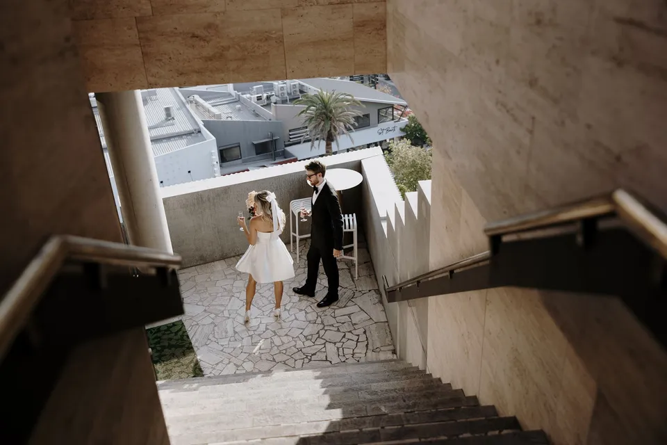 Danielle and Adam seen from above at the foot of a stone staircase, at The Calile Hotel in Fortitude Valley, Brisbane, for an Elopement Collective elopement. Photo by George Bowden.
