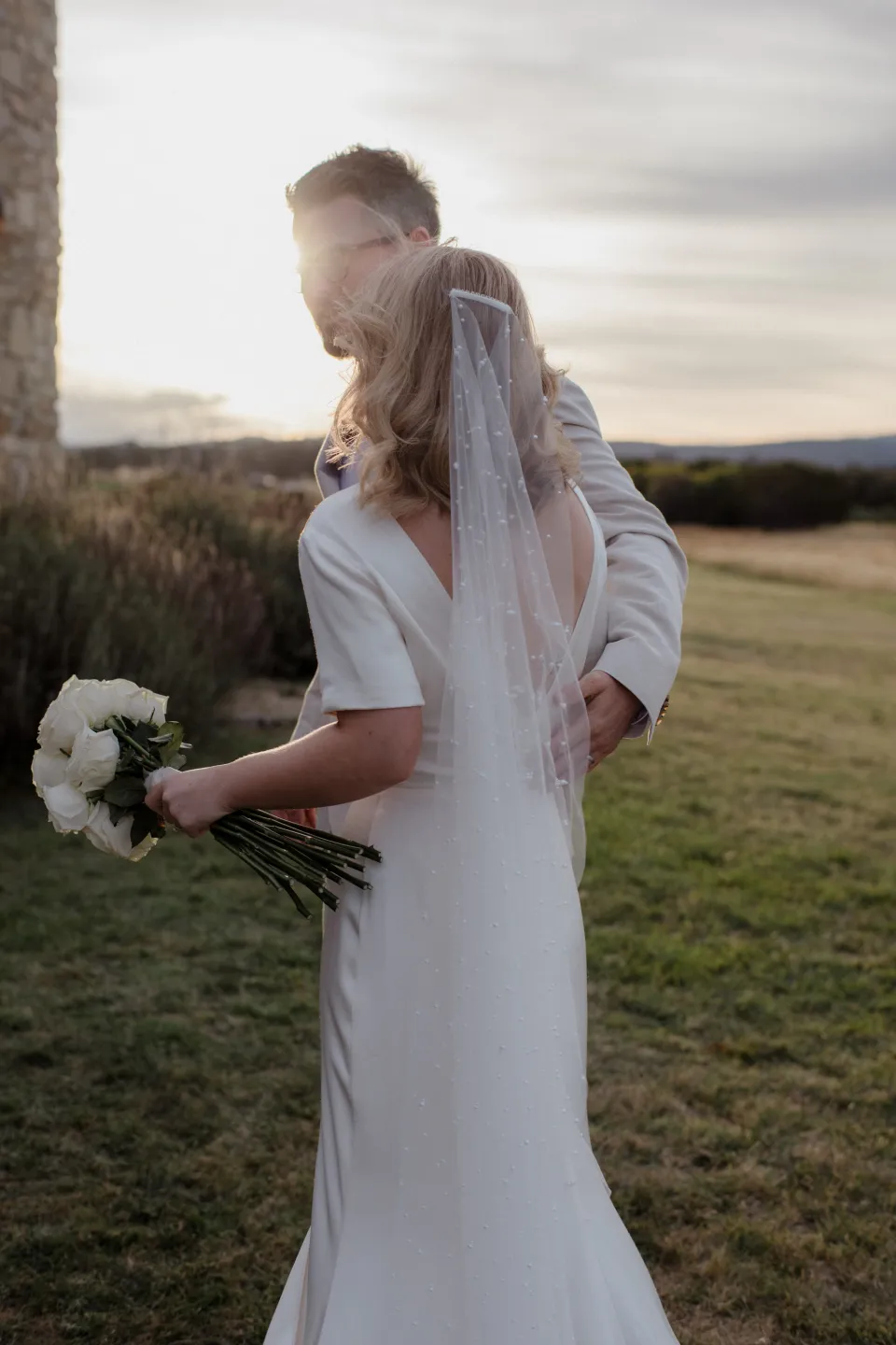 Jack holding Jemmah as they stand beside the coastal meadow, at Thalia Haven on the East Coast of Tasmania, Australia, for an Elopement Collective elopement. Photograph by Joey Willis.