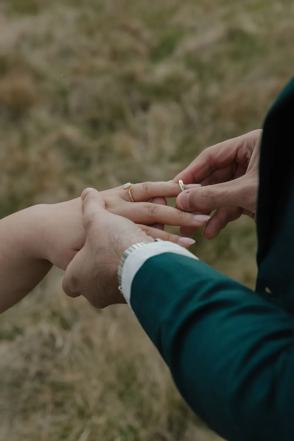 A close view of Adrian placing a wedding ring on Jaeda’s finger during their field ceremony, in the field on the road to Paradise near Glenorchy, in the Queenstown region of New Zealand, for an Elopement Collective Queenstown elopement. Photograph by Bulb Creative.