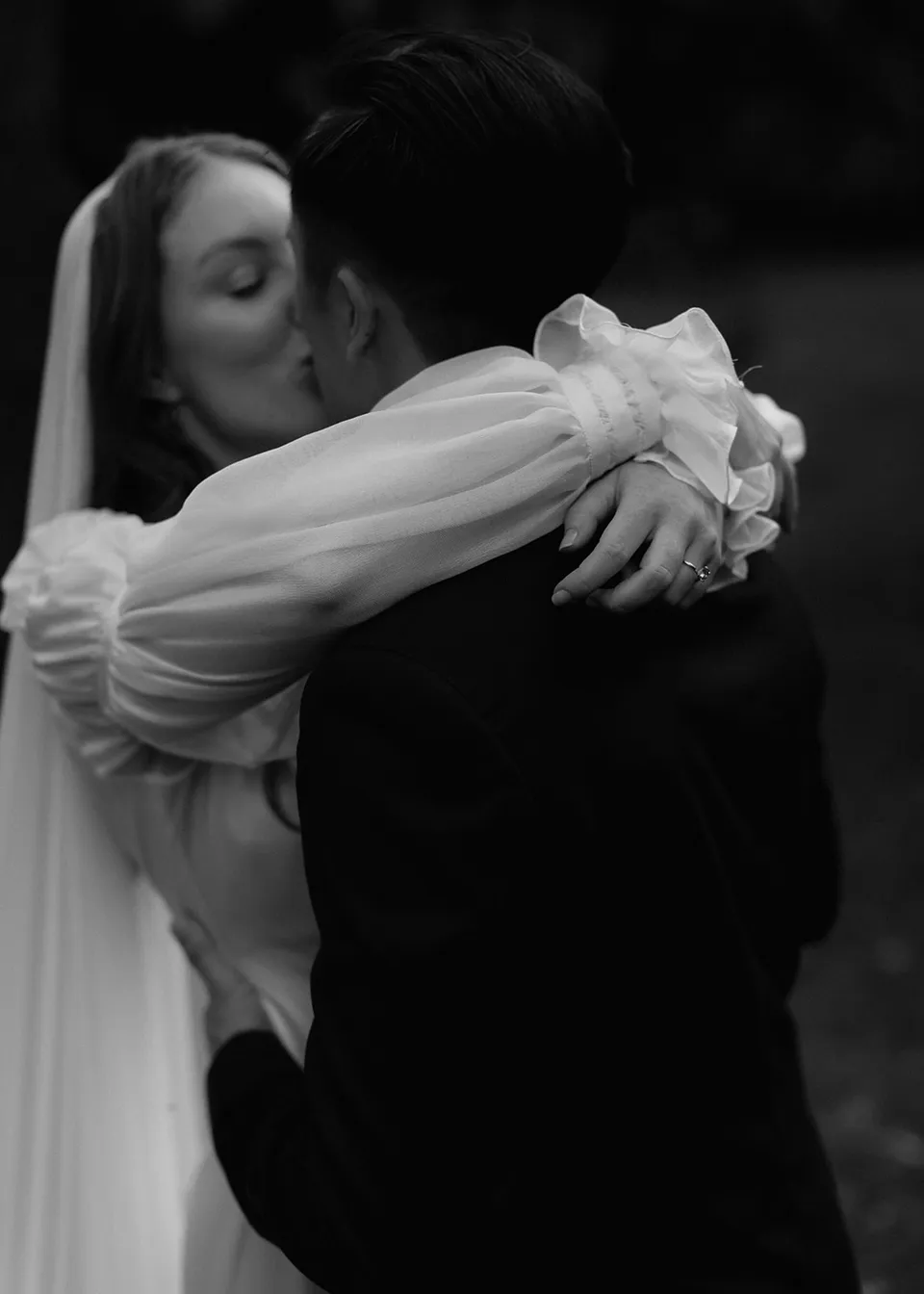 Black-and-white photograph of Elyse embracing Jonathan around his shoulders. At Fig Tree Villa in Ewingsdale, Byron Bay, for an Elopement Collective elopement. Photograph by Bulb Creative.