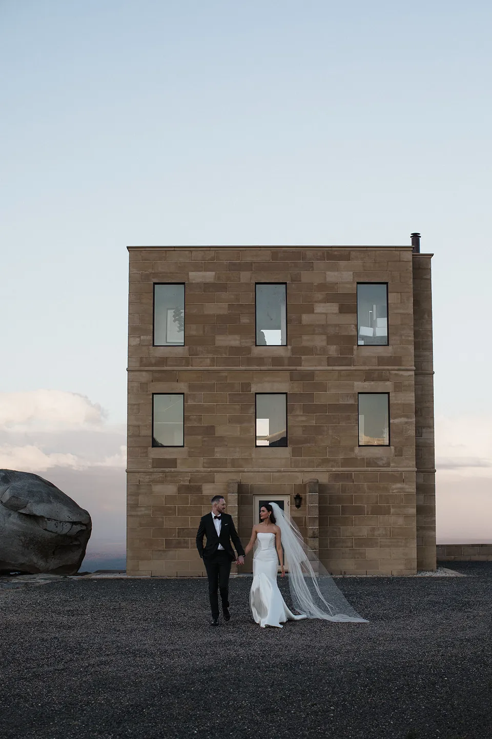 Full-height view of The Keep’s sandstone tower with Meg and Ryan standing together at its doorway. At The Keep on Tasmania’s east coast, for an Elopement Collective elopement. Photograph by Jenna Agius.