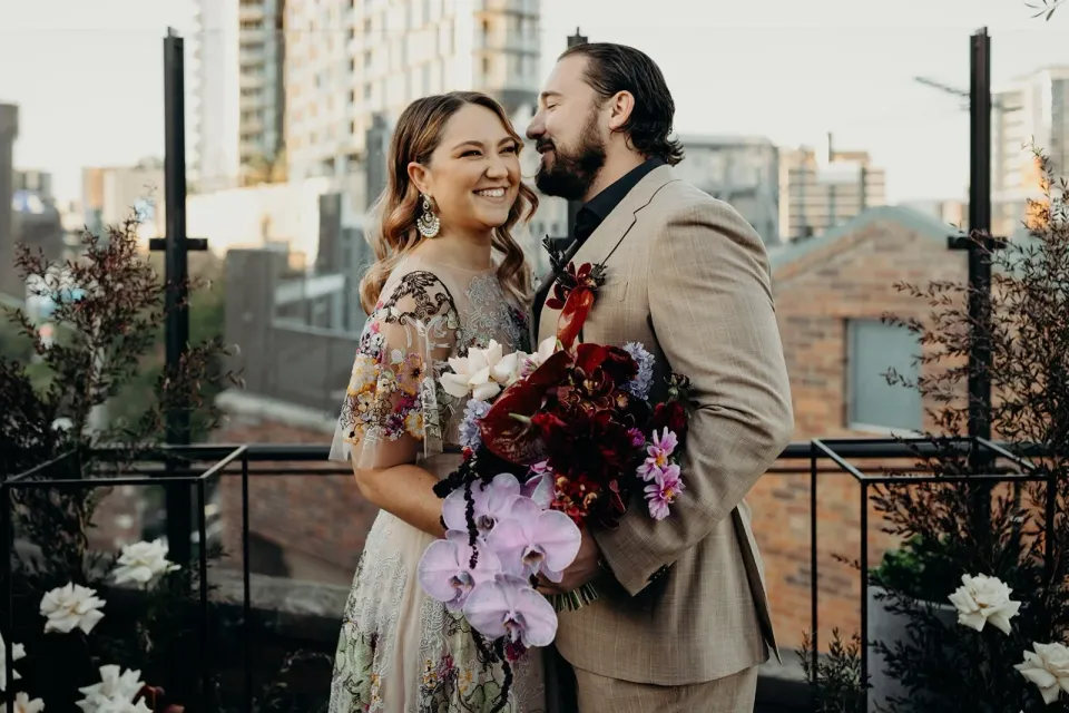 Daniel kissing Victoria’s cheek as she smiles with her bouquet by Mrs Gibbons Flowers, at Agnes Restaurant in Fortitude Valley, Brisbane, for an Elopement Collective elopement. Photo by Tessa Shannon.
