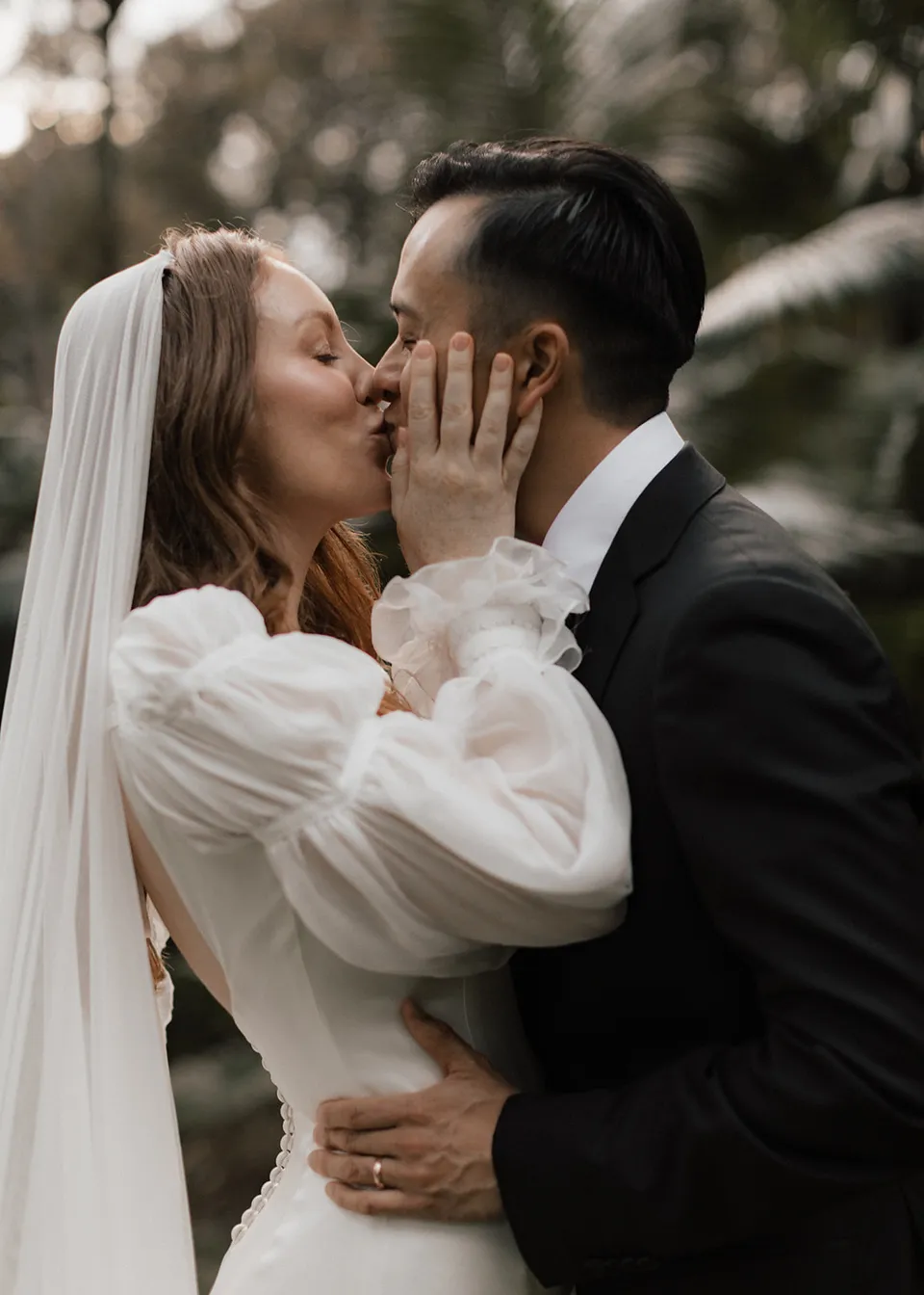 Elyse holding Jonathan's face as they kiss in the garden. At Fig Tree Villa in Ewingsdale, Byron Bay, for an Elopement Collective elopement. Photograph by Bulb Creative.