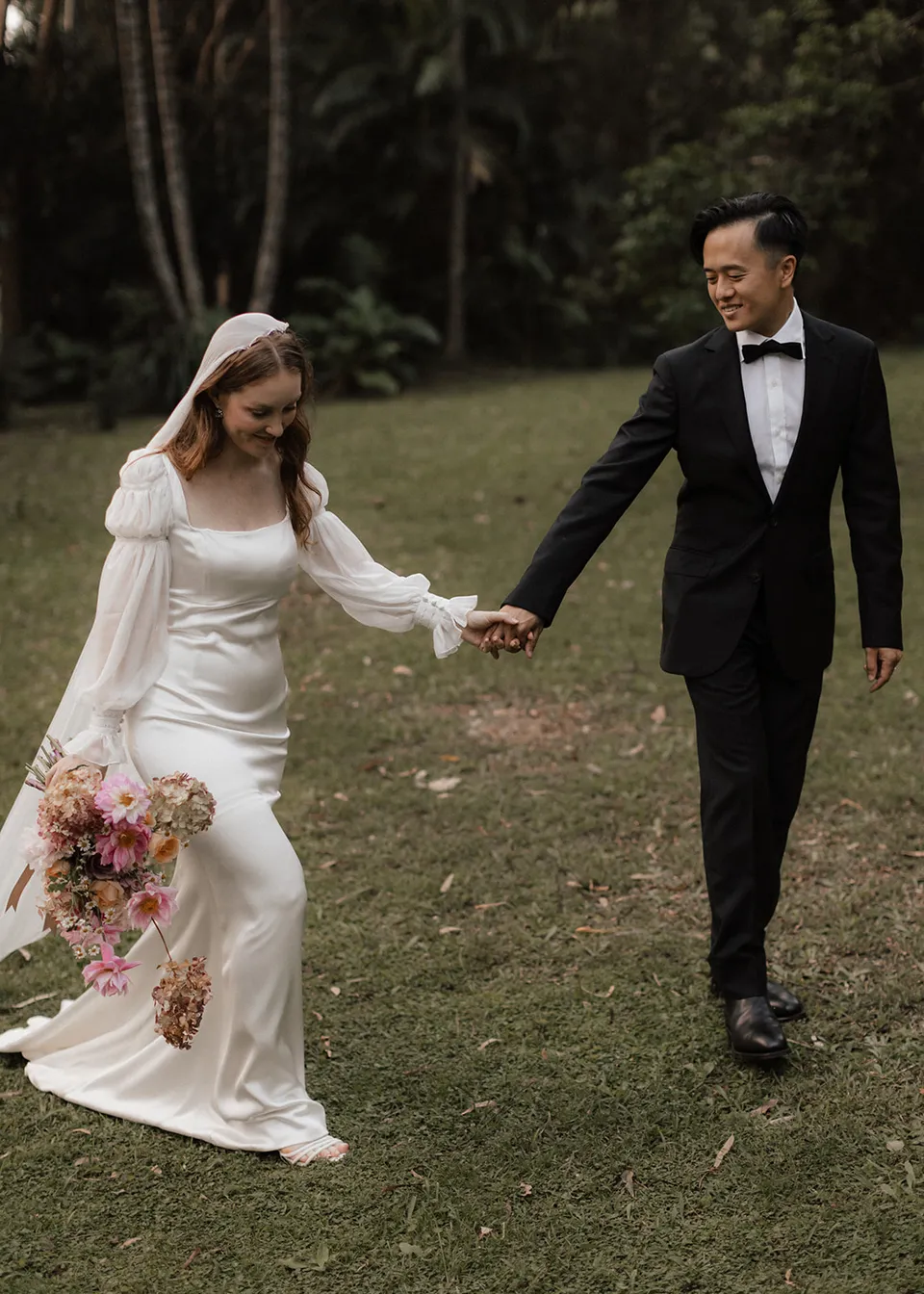 Elyse and Jonathan smiling at each other while walking through the garden. At Fig Tree Villa in Ewingsdale, Byron Bay, for an Elopement Collective elopement. Photograph by Bulb Creative.