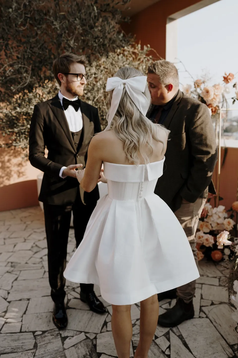 Josh Withers leading Danielle and Adam’s terrace ceremony beside the floral arrangements by Mrs Gibbons Florals, at The Calile Hotel in Fortitude Valley, Brisbane, for an Elopement Collective elopement. Photo by George Bowden.