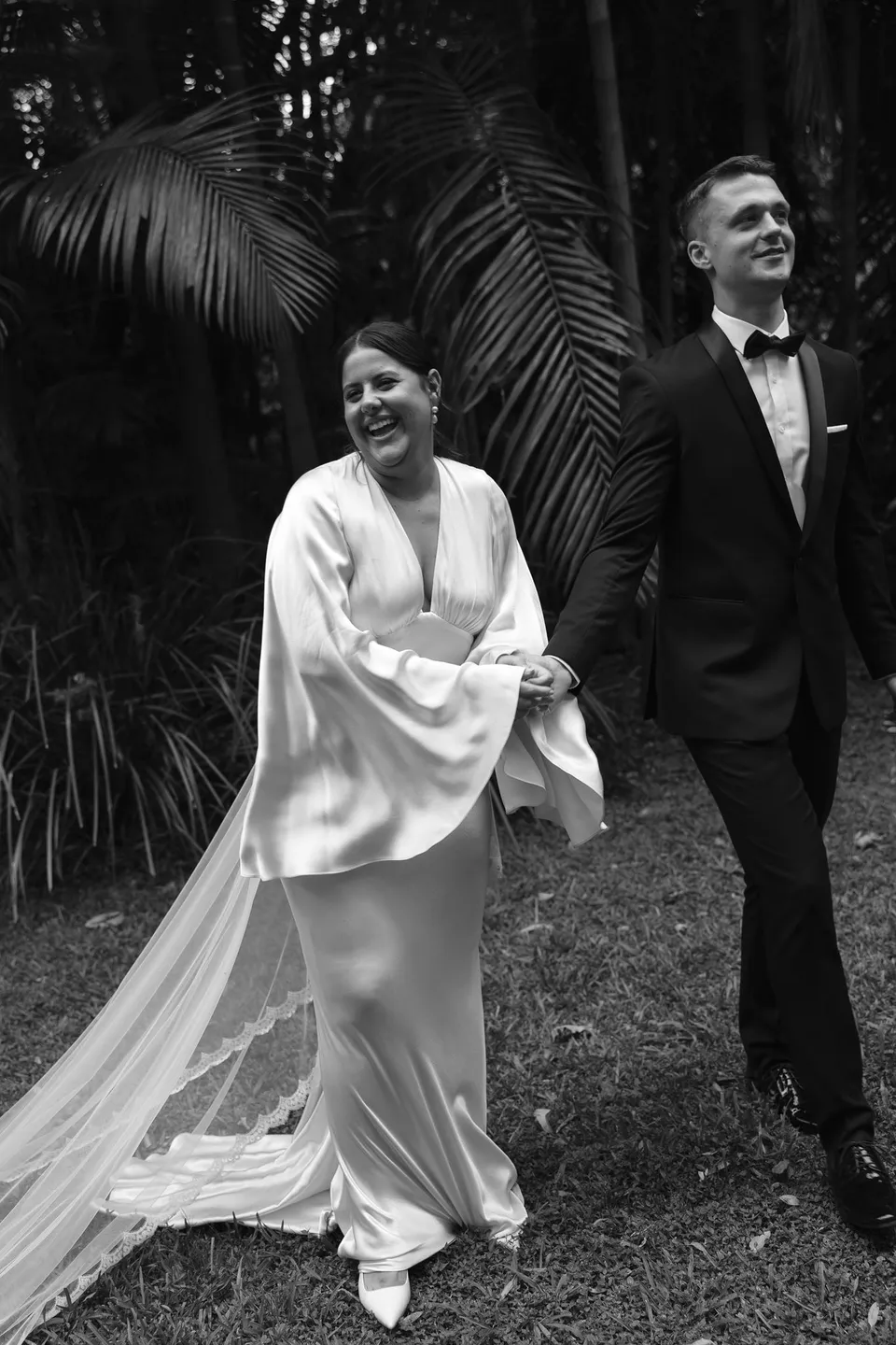 Black-and-white photograph of Laura and Matthew walking together through the garden. At Fig Tree Villa in Ewingsdale, Byron Bay, for an Elopement Collective elopement. Photograph by George Bowden.
