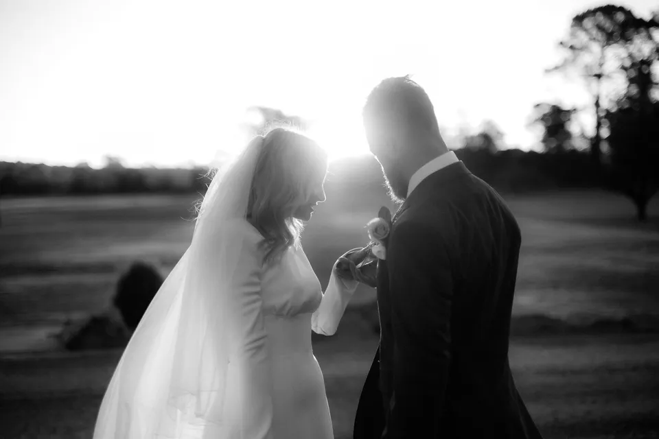 Black and white close-up of Kaitlyn and Russell facing one another in bright backlight. At Piermont Retreat on Tasmania’s east coast, for an Elopement Collective elopement. Photograph by Omar of By The Wilde.