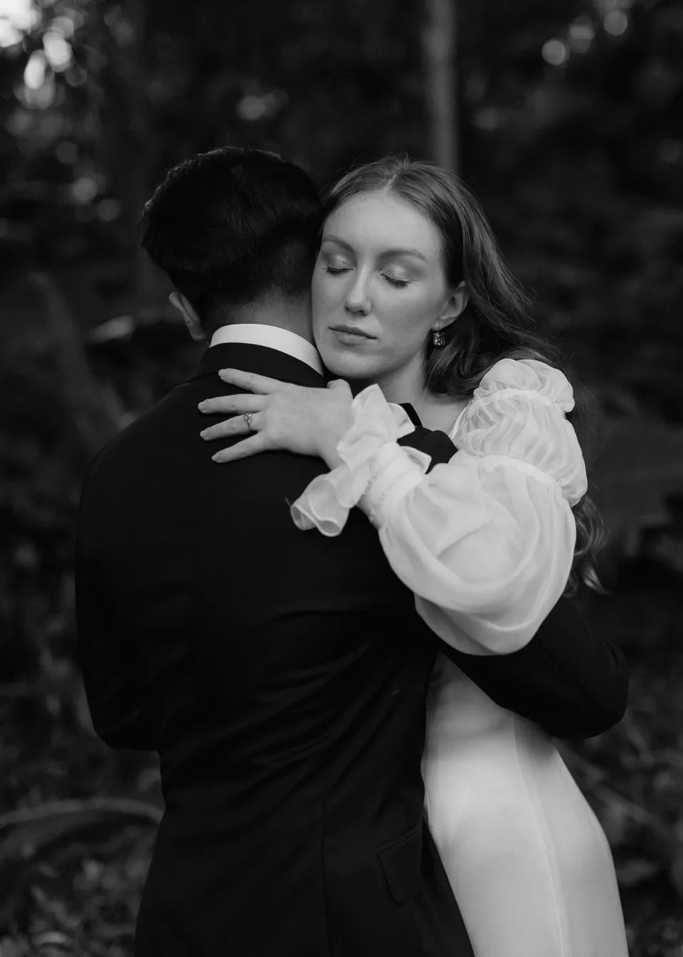 Black-and-white photograph of Elyse resting against Jonathan's shoulder. At Fig Tree Villa in Ewingsdale, Byron Bay, for an Elopement Collective elopement. Photograph by Bulb Creative.