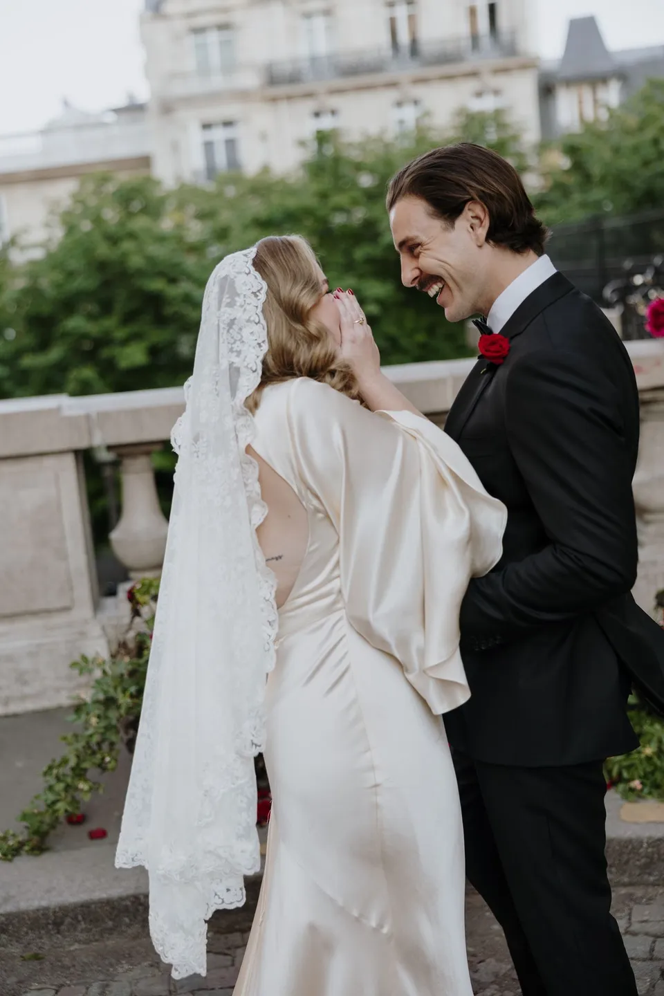 Samuel reading from an open vow book while holding Kara’s hand as she smiles up at him, at Avenue de Camoëns in Paris, France, during an Elopement Collective elopement. Photograph by George Bowden.