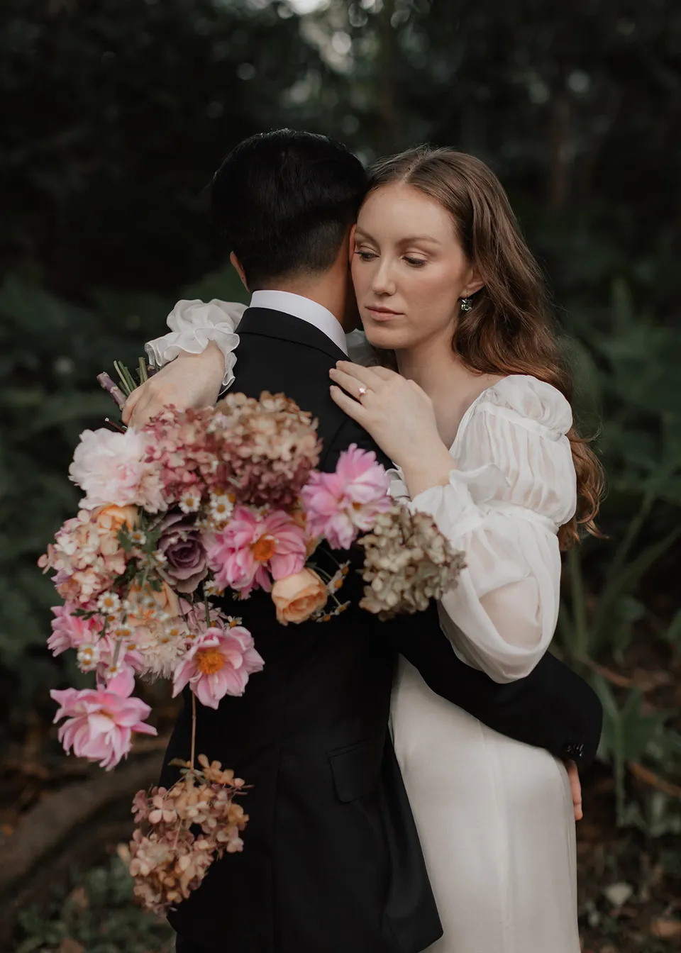 Close portrait of Elyse holding her bouquet as she leans into Jonathan, with flowers by The Perfect Party Co. At Fig Tree Villa in Ewingsdale, Byron Bay, for an Elopement Collective elopement. Photograph by Bulb Creative.