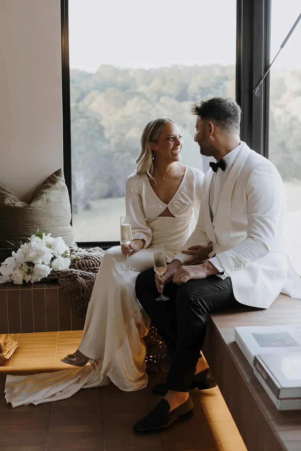 Gabrielle and Greg sitting close together on the cabin’s window seat with her bouquet beside them, at Roundhill Retreat in Obi Obi, Sunshine Coast Hinterland, Queensland, for an Elopement Collective elopement. Photo by George Bowden.