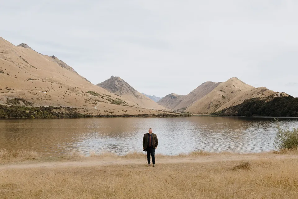 Celebrant Josh Withers looking across the still water towards the surrounding mountains, at Moke Lake in Queenstown, New Zealand, for an Elopement Collective Queenstown elopement. Photo by George Bowden.