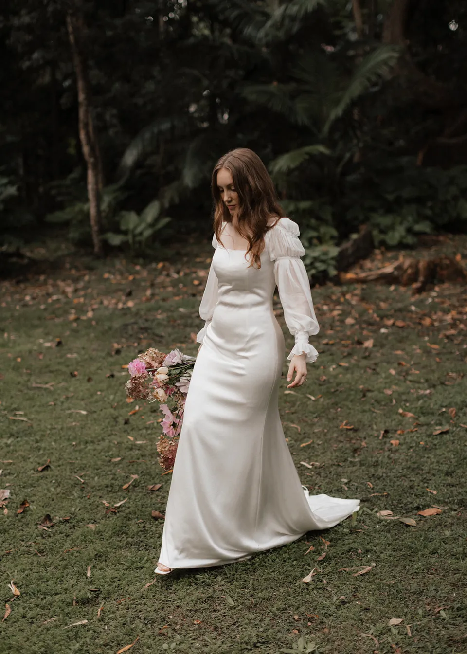 Elyse looking down as she walks beside the trees. At Fig Tree Villa in Ewingsdale, Byron Bay, for an Elopement Collective elopement. Photograph by Bulb Creative.