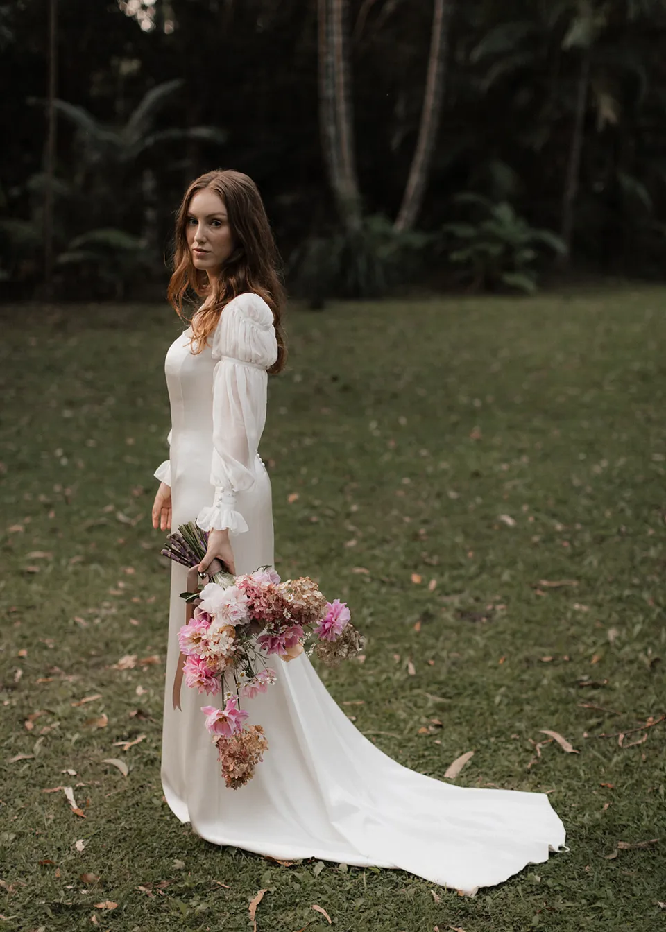 Elyse holding her bouquet beside her long white dress in the garden, with flowers by The Perfect Party Co. At Fig Tree Villa in Ewingsdale, Byron Bay, for an Elopement Collective elopement. Photograph by Bulb Creative.