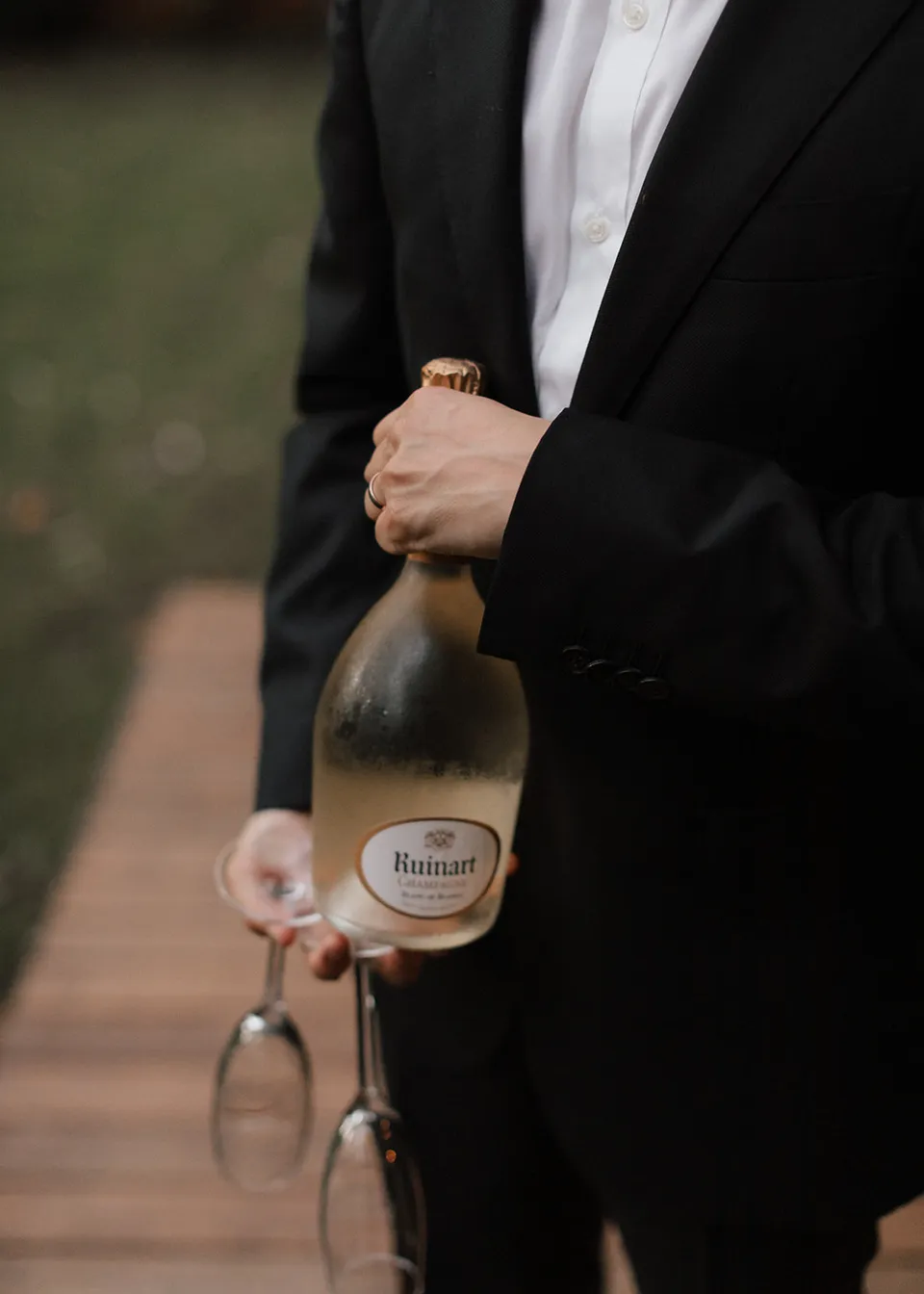 Jonathan opening a bottle of sparkling wine beside two glasses. At Fig Tree Villa in Ewingsdale, Byron Bay, for an Elopement Collective elopement. Photograph by Bulb Creative.