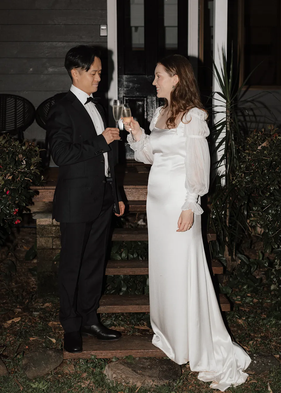 Elyse and Jonathan raising their glasses together outside the cottage. At Fig Tree Villa in Ewingsdale, Byron Bay, for an Elopement Collective elopement. Photograph by Bulb Creative.