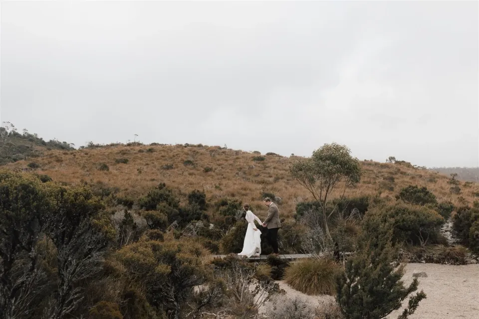A couple embrace on a small bridge surrounded by alpine shrubs.