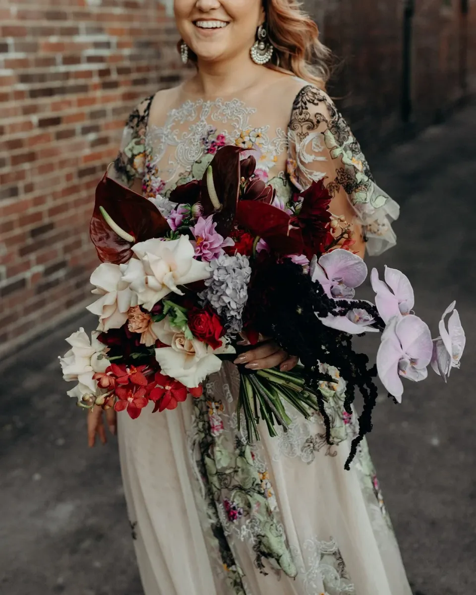 Victoria smiling with her bouquet of purple orchids and burgundy flowers by Mrs Gibbons Flowers, in Fortitude Valley, Brisbane, for an Elopement Collective elopement. Photo by Tessa Shannon.