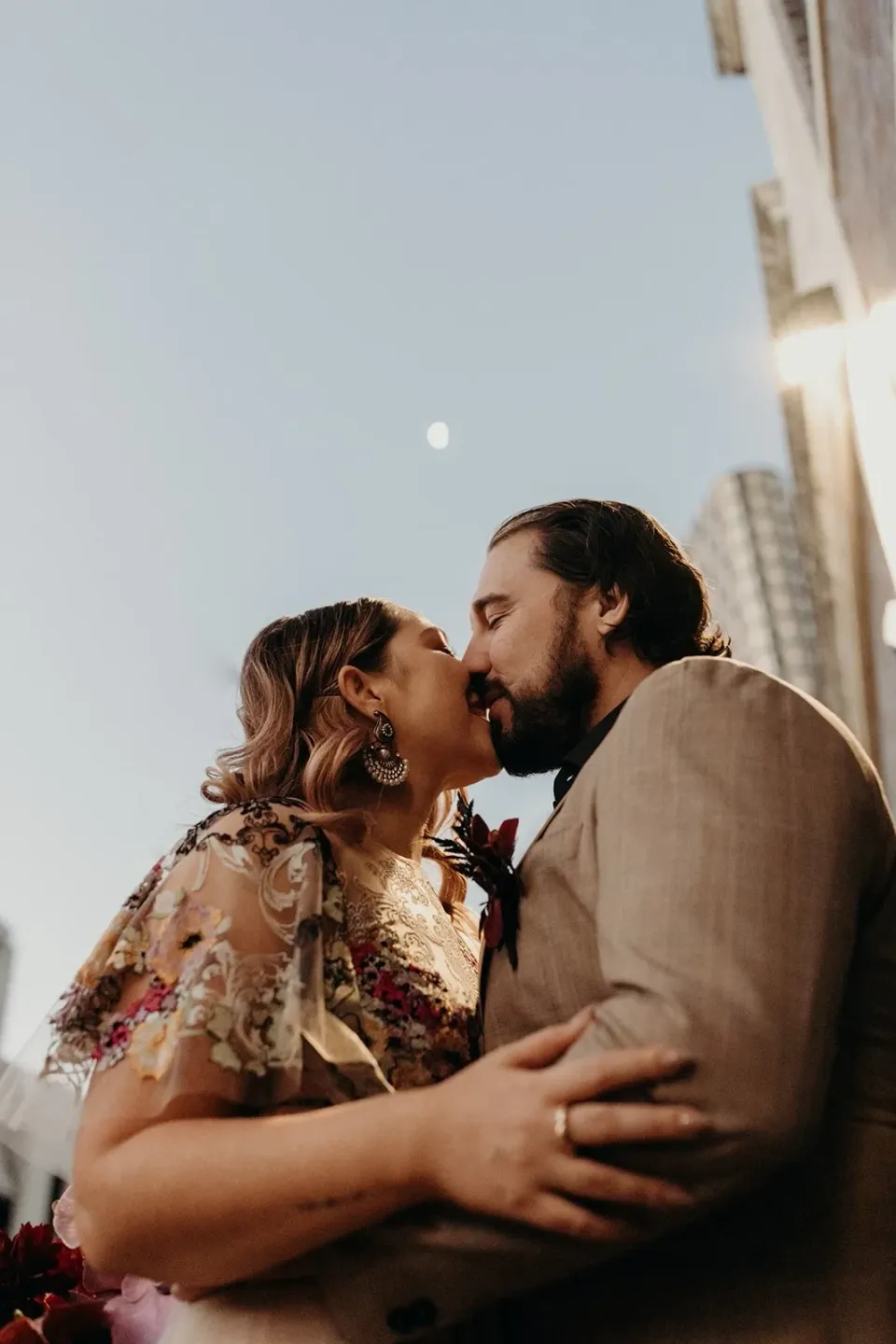 Victoria and Daniel kissing beside a black roller door with city buildings behind them, in Fortitude Valley, Brisbane, for an Elopement Collective elopement. Photo by Tessa Shannon.