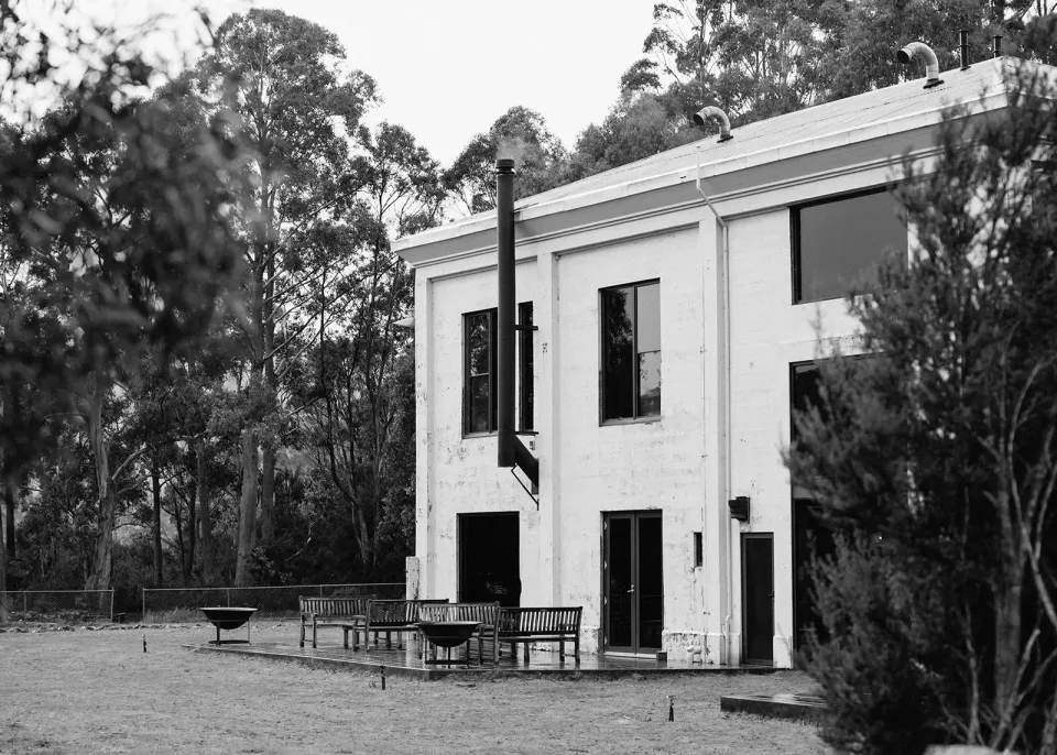 A black-and-white photograph of a two-storey lakeside building surrounded by tall trees.