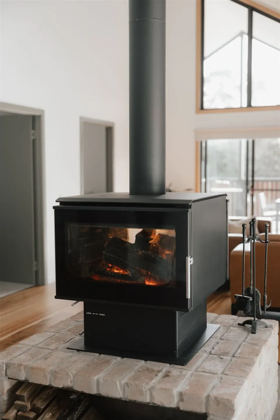 A wood-burning stove glows inside a bright room with timber floors and tall windows.