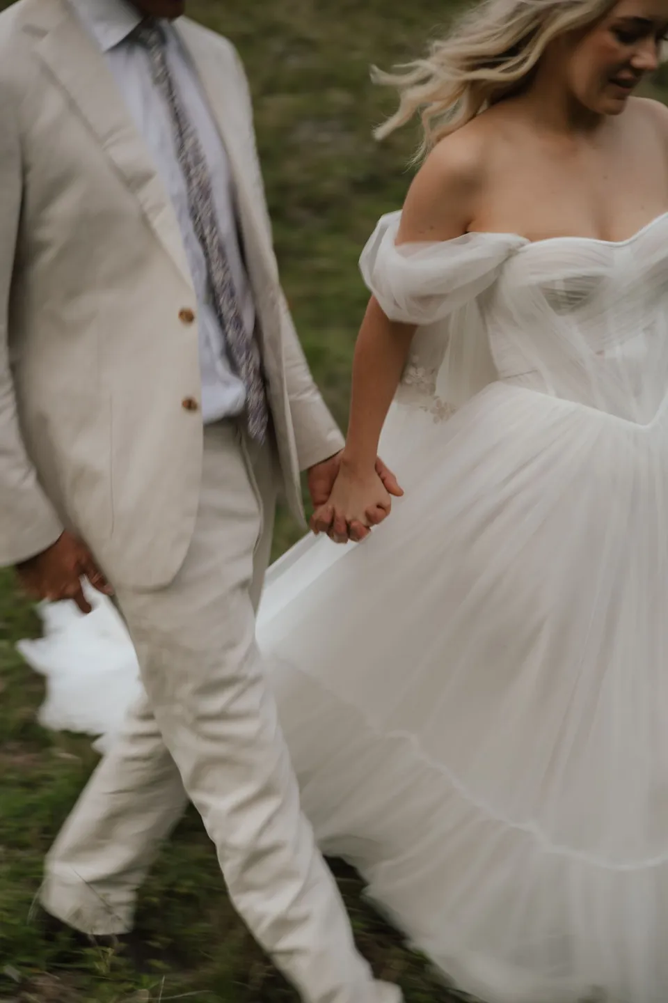 Close-up of Bridget and James holding hands as they walk through the grass. At Cudgera Creek in northern New South Wales, for an Elopement Collective elopement. Photograph by Bulb Creative.