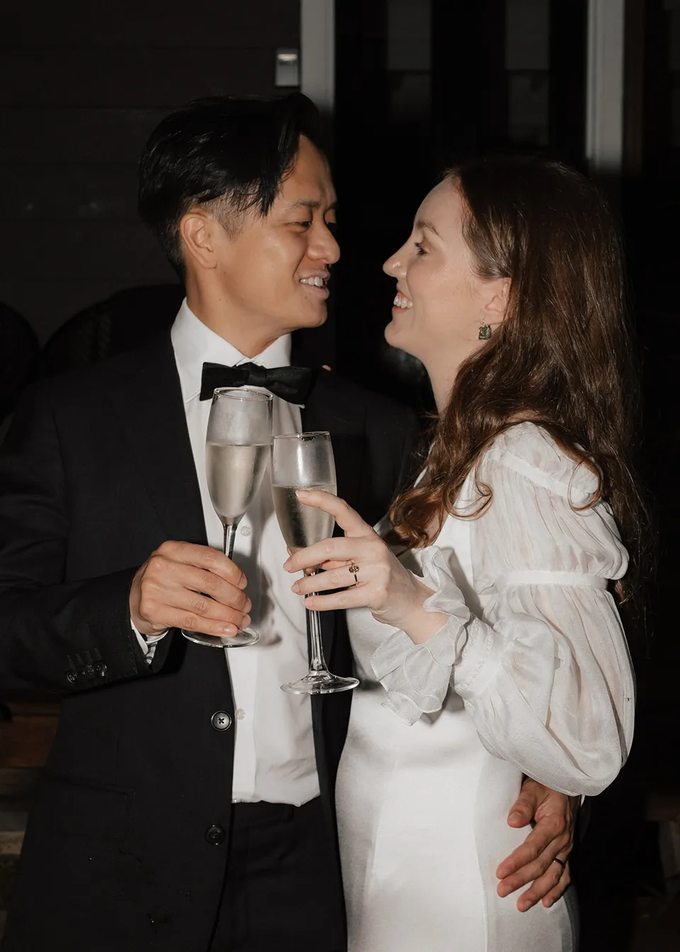 Elyse and Jonathan exchanging a smile with sparkling wine in hand. At Fig Tree Villa in Ewingsdale, Byron Bay, for an Elopement Collective elopement. Photograph by Bulb Creative.
