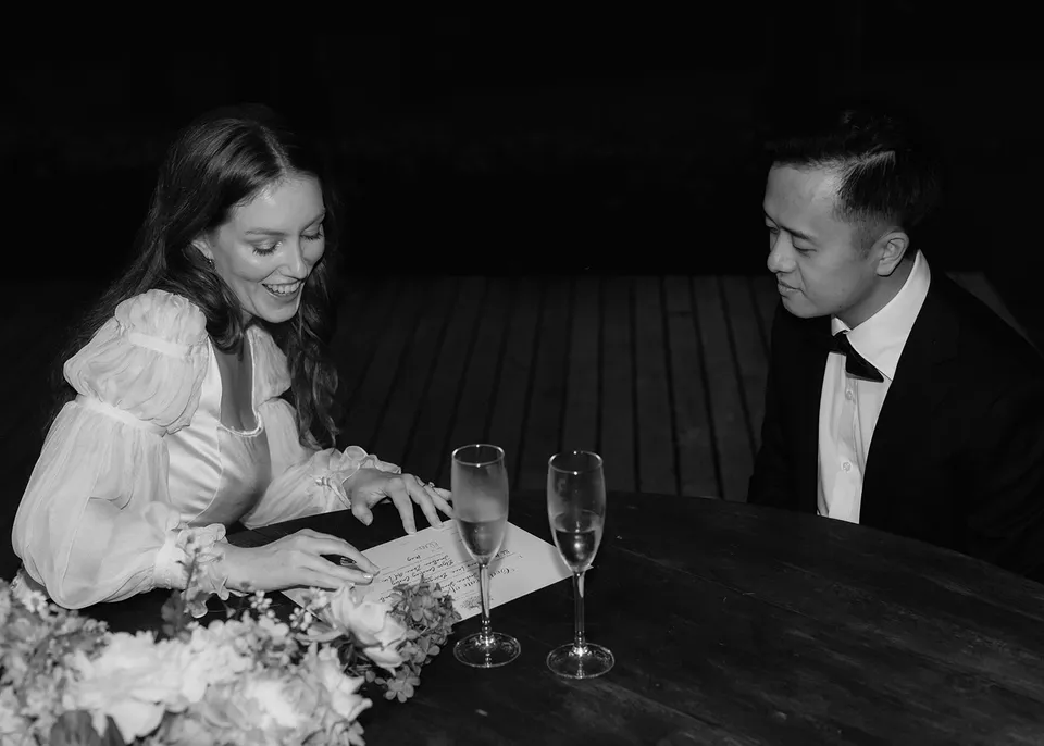 Black-and-white photograph of Elyse smiling as she signs the paperwork. At Fig Tree Villa in Ewingsdale, Byron Bay, for an Elopement Collective elopement. Photograph by Bulb Creative.