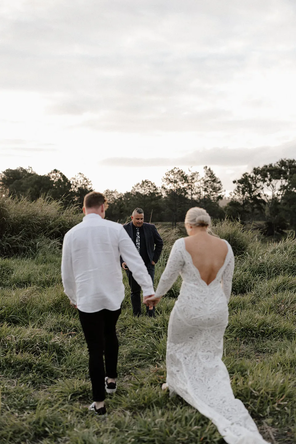 Matt and Laura walking hand in hand through the grass towards celebrant Josh Withers, in the Tweed Valley, NSW, for an Elopement Collective elopement. Photo by Bulb Creative.