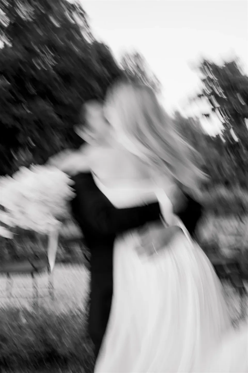 Black-and-white photograph with motion blur of Shelby and Jack kissing, her bouquet by Le Francesche beside them, in Umbria, Italy, for an Elopement Collective elopement. Photo by James from House of Love.