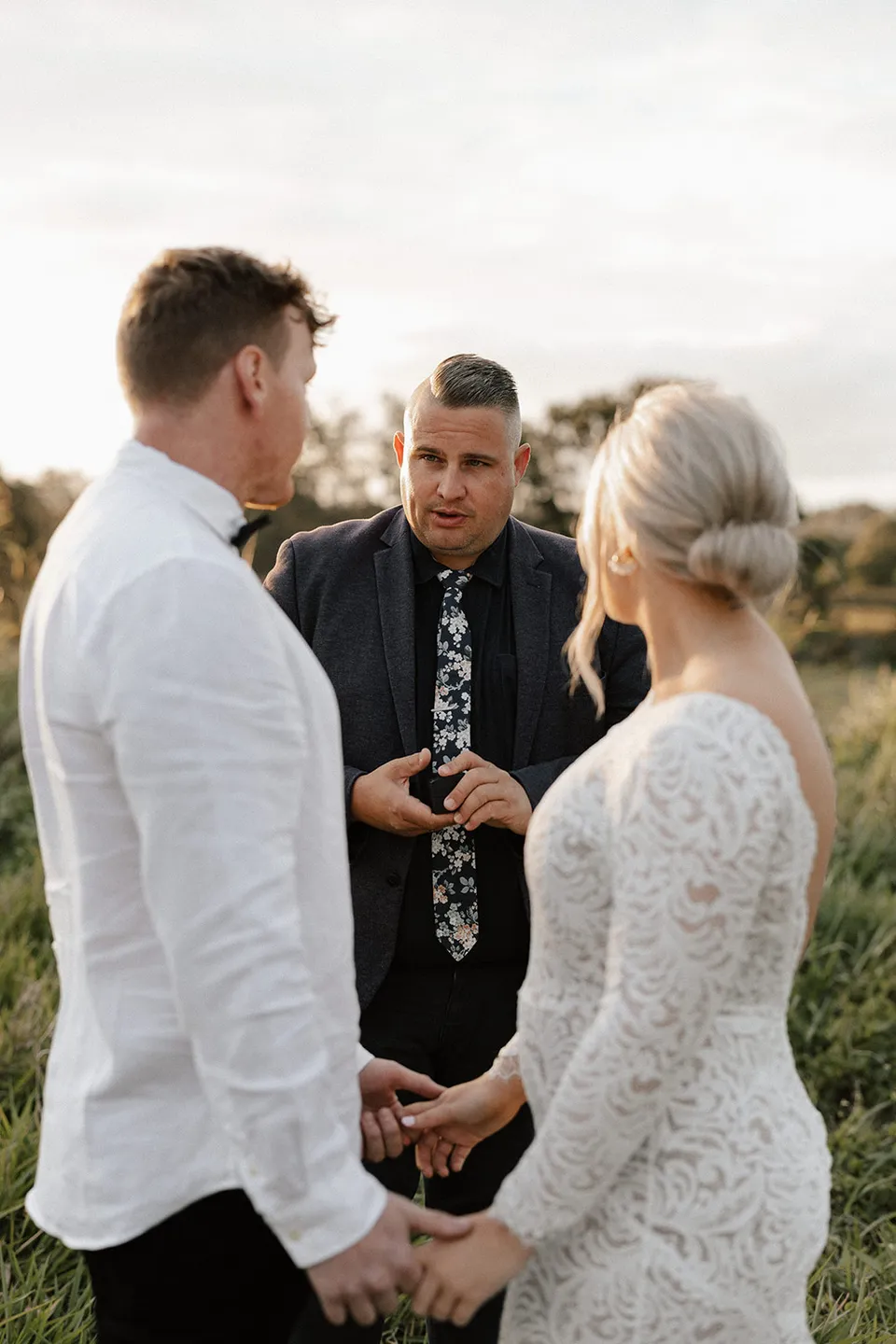 Celebrant Josh Withers speaking to Matt and Laura as they hold hands during their ceremony, in the Tweed Valley, NSW, for an Elopement Collective elopement. Photo by Bulb Creative.