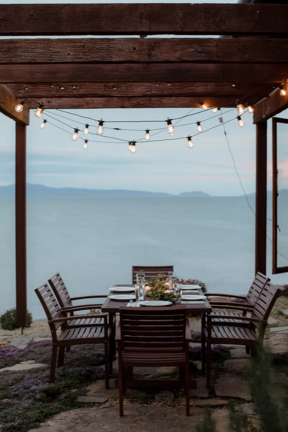 A candlelit dining table beneath festoon lights beside Great Oyster Bay, at Thalia Haven on the East Coast of Tasmania, Australia, for an Elopement Collective elopement. Photograph by Joey Willis.