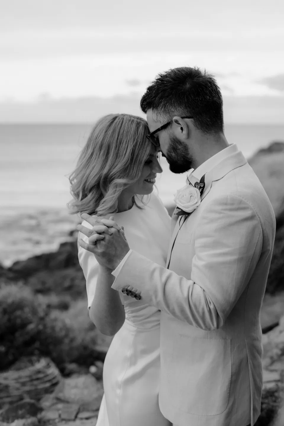 Black and white close portrait of the couple kissing beside the bay, at Thalia Haven on the East Coast of Tasmania, Australia, for an Elopement Collective elopement. Photograph by Joey Willis.